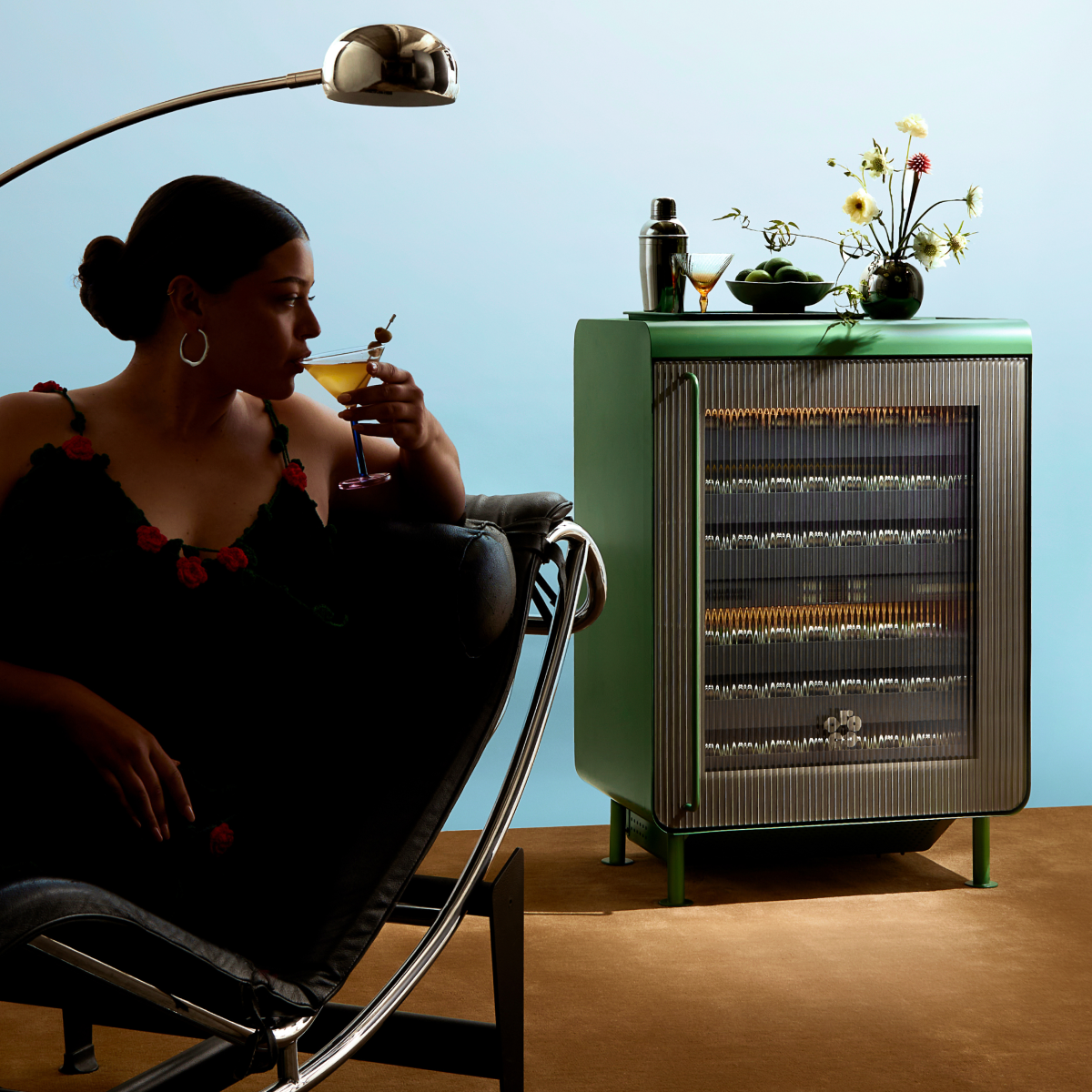Woman sipping a cocktail next to a fully stocked closed Green Rocco.